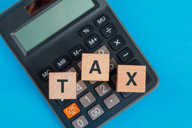 wooden scrabble pieces spelt out as tax being placed on top of a calculator